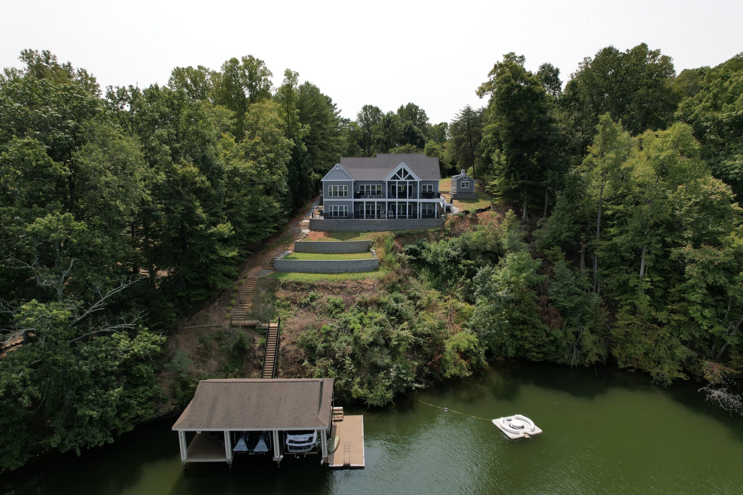 Aerial view showing custom home on sloped lot with terraced yard, dock, and boathouse on Smith Mountain Lake