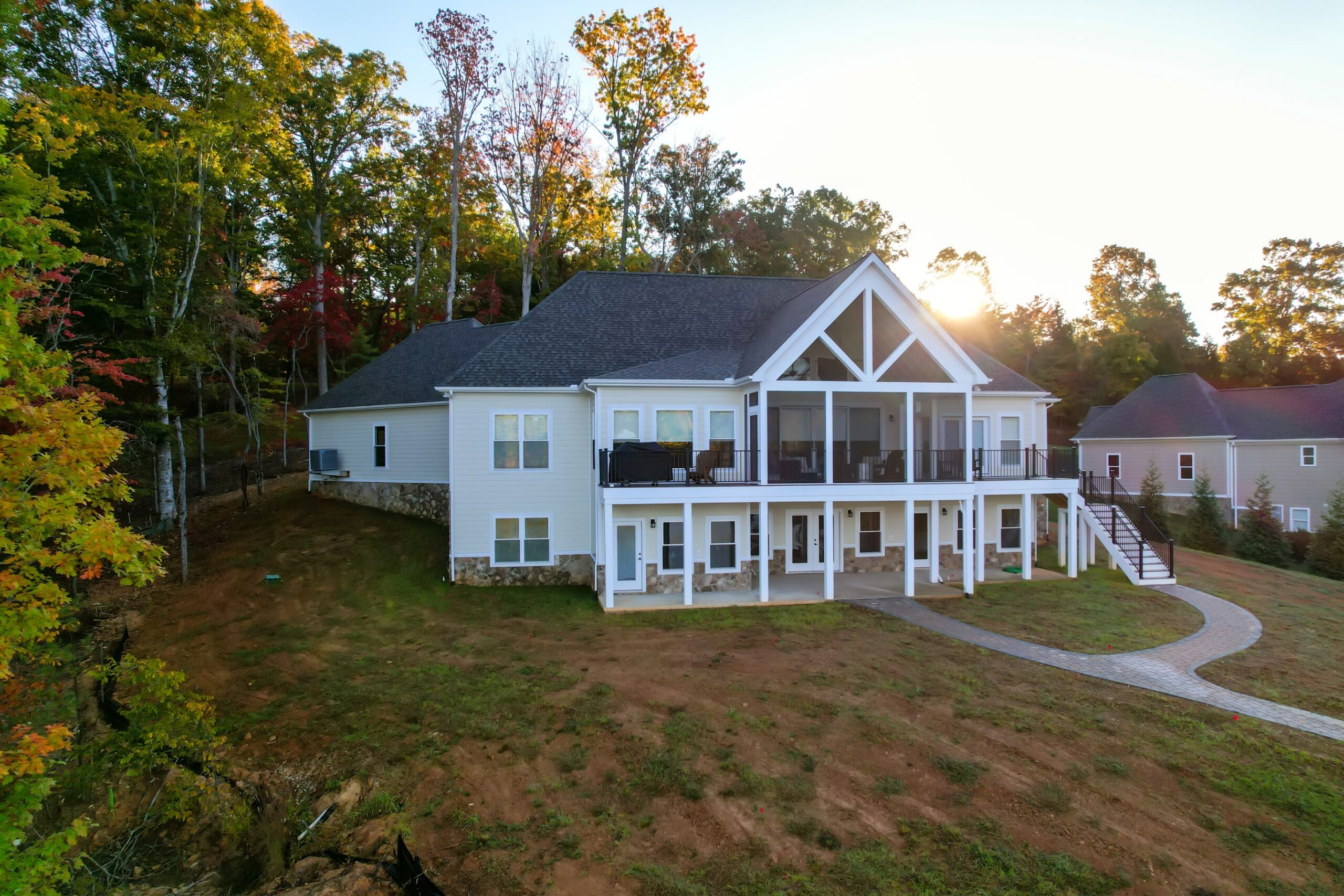 Lake side showing screened gable porch, open deck, stone veneer walkout lower level, and paver walkway