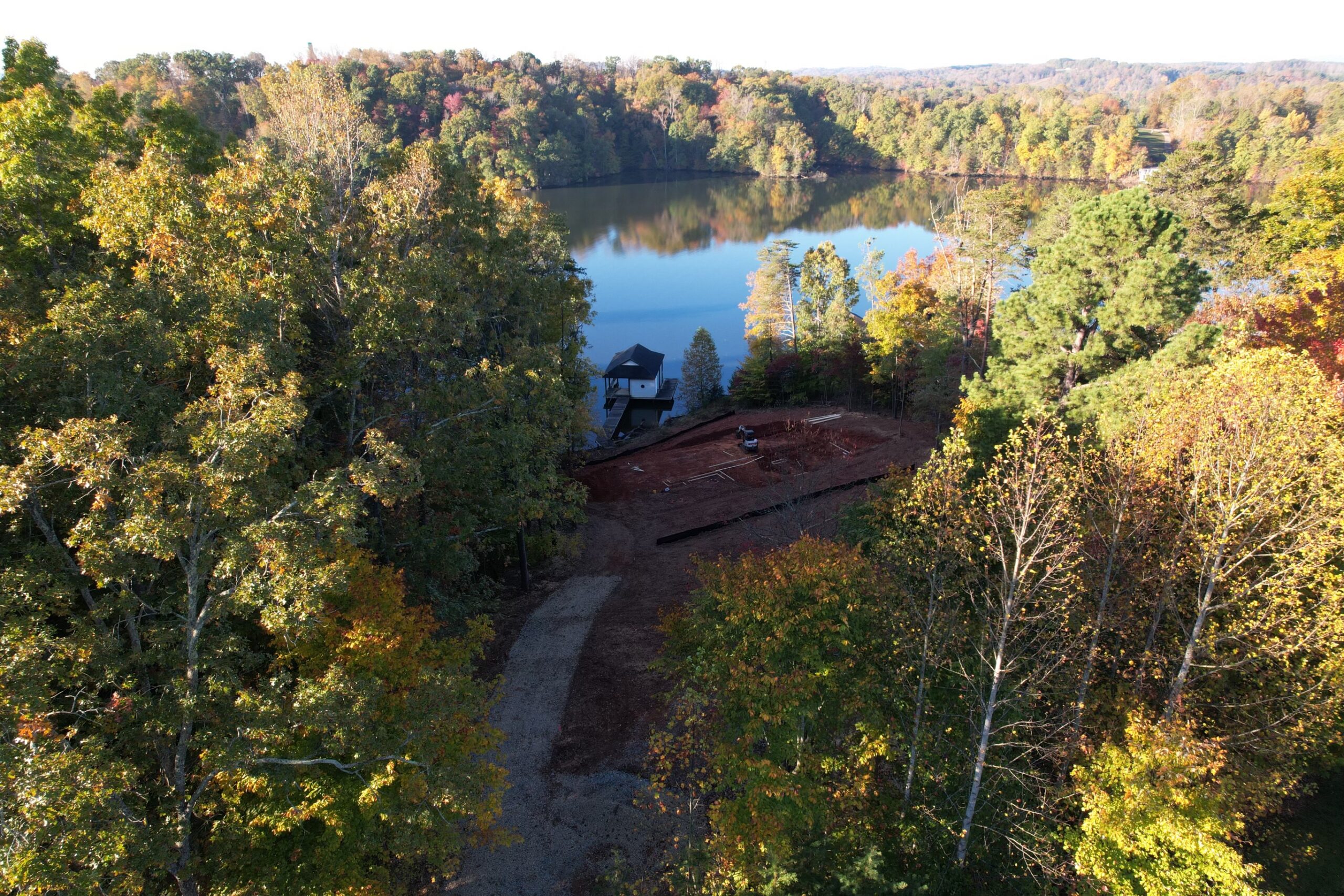 Aerial view of lakefront lot during early construction, showing cleared site, gravel drive, and dock on Smith Mountain Lake